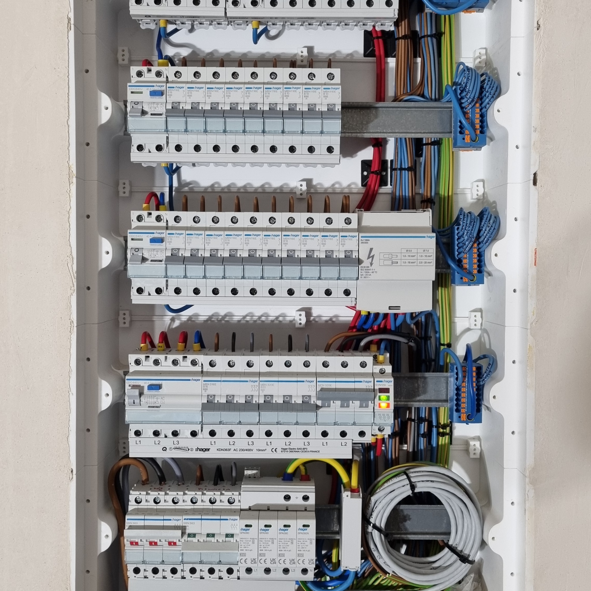 Rozdzielnica elektryczna Hager z zainstalowanymi bezpiecznikami i okablowaniem. Widoczne przewody w różnych kolorach i oznaczenia na urządzeniach.