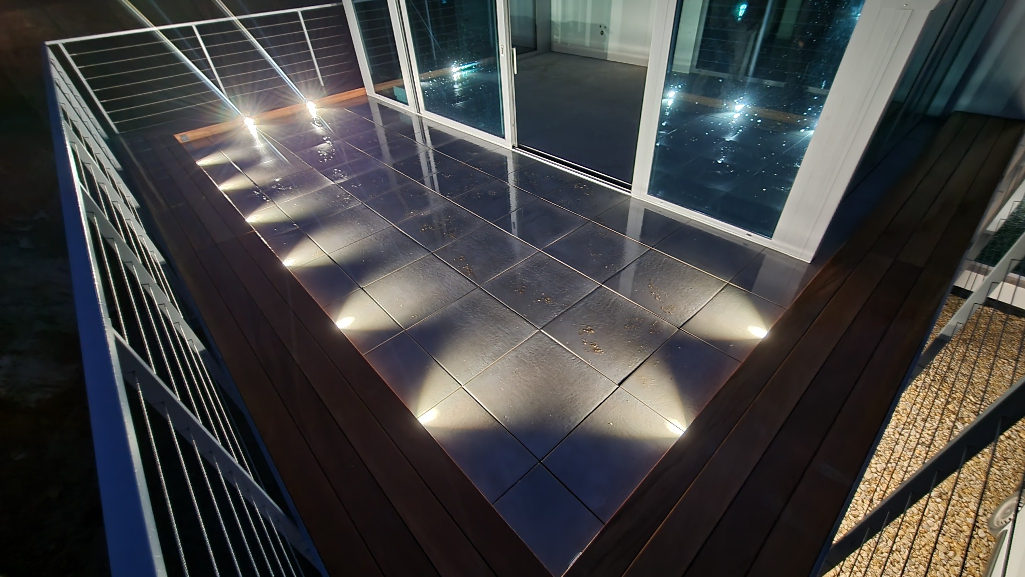 Nowoczesny balkon z podświetlaną podłogą z płytek, widok z góry. Metalowa balustrada, przesuwne okna balkonowe. Nocne oświetlenie punktowe.