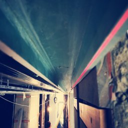 PreciseHomeRenowation - Montaż sufitu podwieszanego: widok z dołu na konstrukcję z profili, poziomica laserowa wyznacza linię, a pracownik trzyma element płyty. W tle widoczne materiały budowlane.