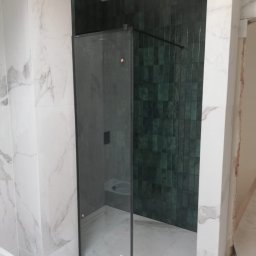 Nowoczesna kabina prysznicowa z czarnym profilem, wykończona eleganckimi zielonymi płytkami oraz dużymi płytami imitującymi marmur. Przykład precyzyjnego montażu i stylowego wykończenia łazienki przez Precise Home Renovation.