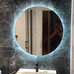 Nowoczesna łazienka z eleganckim wykończeniem. Wykonano precyzyjny montaż płytek wielkoformatowych w ciemnym marmurowym stylu. Zainstalowano podświetlane lustro LED oraz szafkę z umywalką nablatową w stylu dębowym.