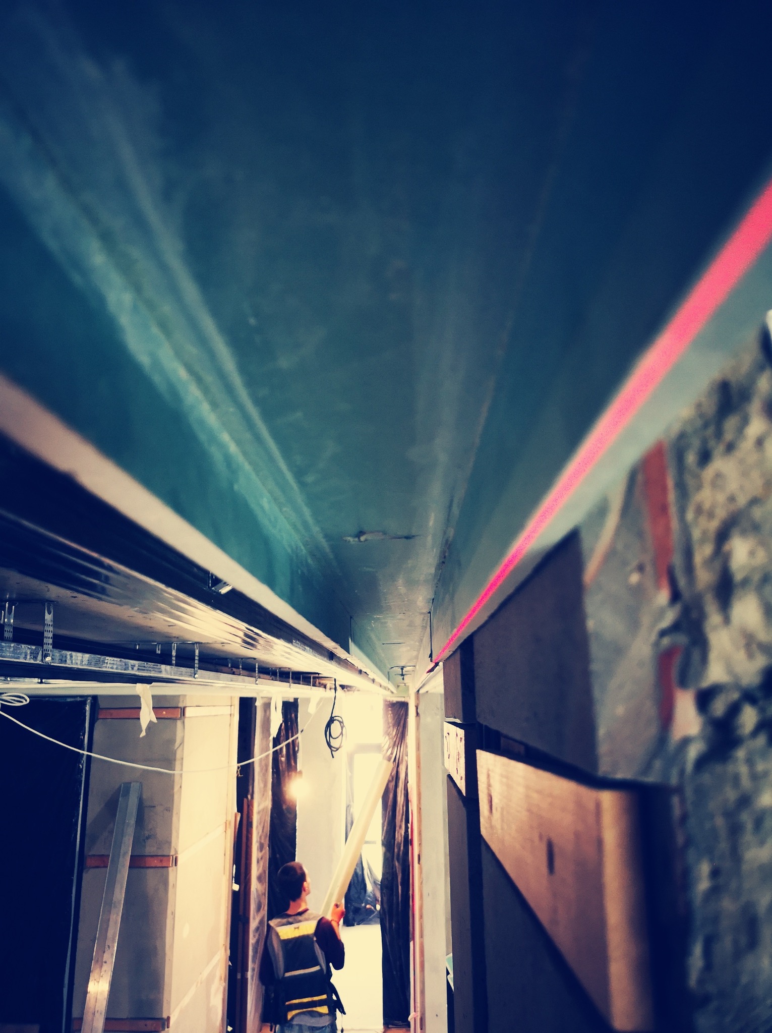 Montaż sufitu podwieszanego: widok z dołu na konstrukcję z profili, poziomica laserowa wyznacza linię, a pracownik trzyma element płyty. W tle widoczne materiały budowlane.