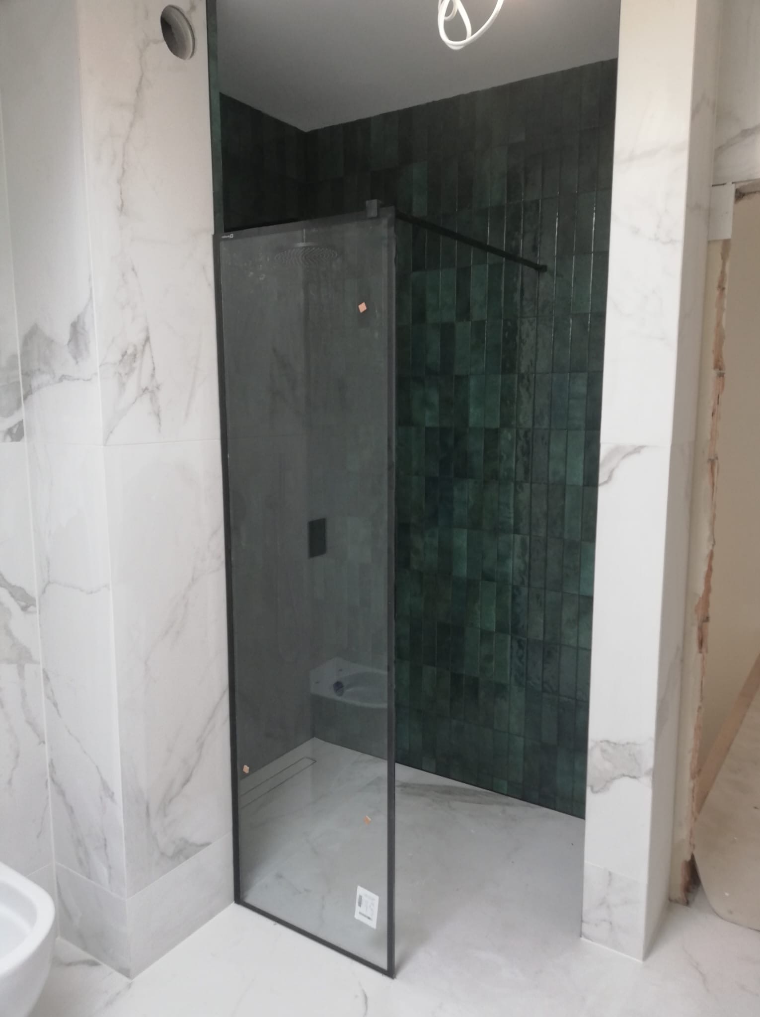 Łazienka z kabiną prysznicową: czarne profile, zielone płytki i marmurowe płyty. Widoczne wykończenie i montaż.