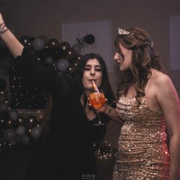 Hamad photography - Dwie kobiety świętują na tle dekoracji balonowych i subtelnych światełek. Jedna pije drinka przez słomkę, druga ma tiarę. Ujęcie z imprezy okolicznościowej.