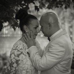 Hamad photography - Czarno-białe zbliżenie nowożeńców: kobieta w koronkowej sukni i mężczyzna w jasnym garniturze, patrzący sobie w oczy pod drzewem.