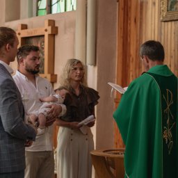 Hamad photography - Uroczystość chrztu w kościele: ksiądz w zielonej szacie, rodzina z dzieckiem przy drewnianej chrzcielnicy. Jasne wnętrze, świeca paschalna.