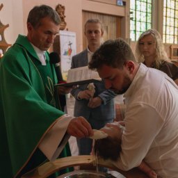 Hamad photography - Ksiądz w zielonej szacie udziela sakramentu chrztu dziecku w kościele. W tle rodzice i ministrant.