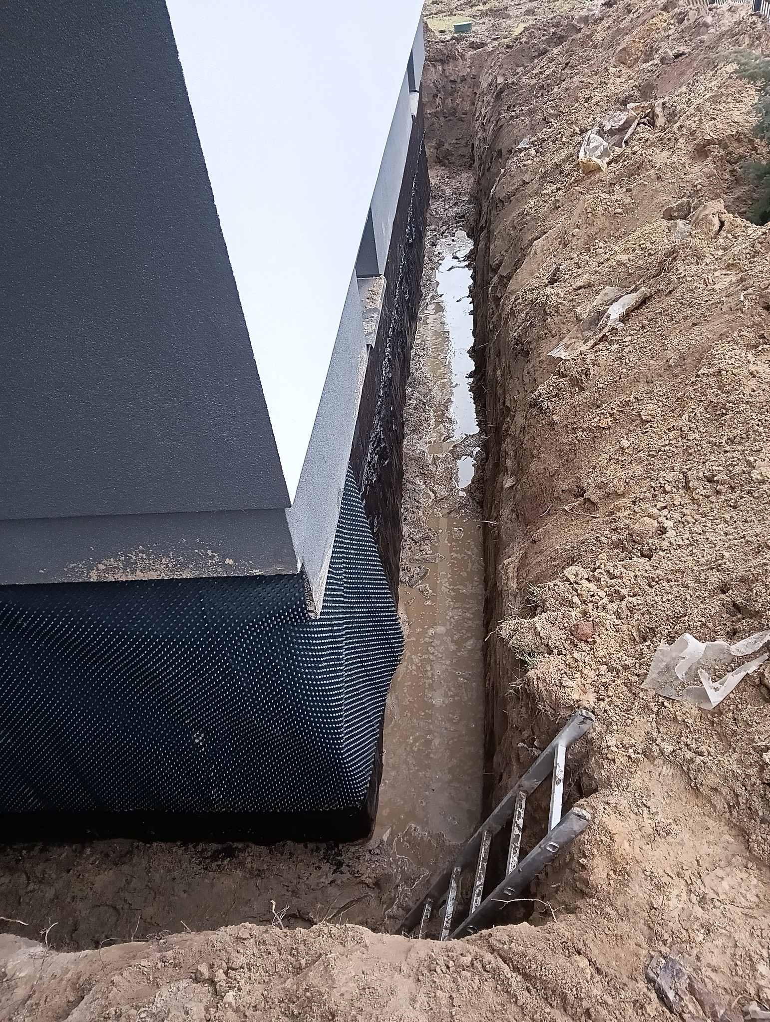 Wykop z izolacją fundamentów budynku, widoczna woda w wykopie i drabina. Grunt piaszczysty.