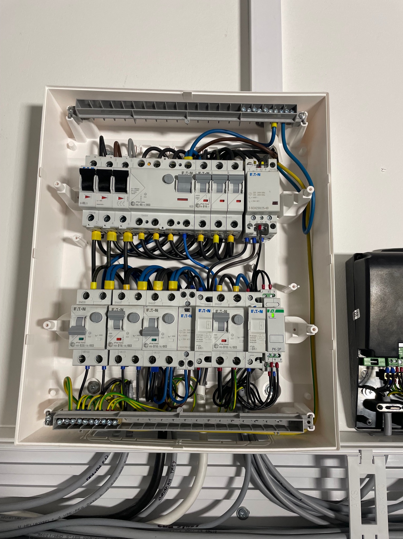 Rozdzielnica elektryczna marki Eaton w białej obudowie, z widocznymi bezpiecznikami i okablowaniem w kolorach niebieskim, żółtym i czarnym. Widoczne kable wchodzące do skrzynki.