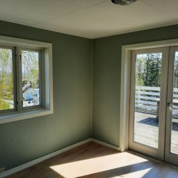 GKM Gracjan Kaźmierski - Pomalowane na zielono wnętrze z oknem i wyjściem na taras w Zgierzu. Widok na zieleń za oknem i na tarasie. Świeżo odmalowane ściany i drewniana podłoga.