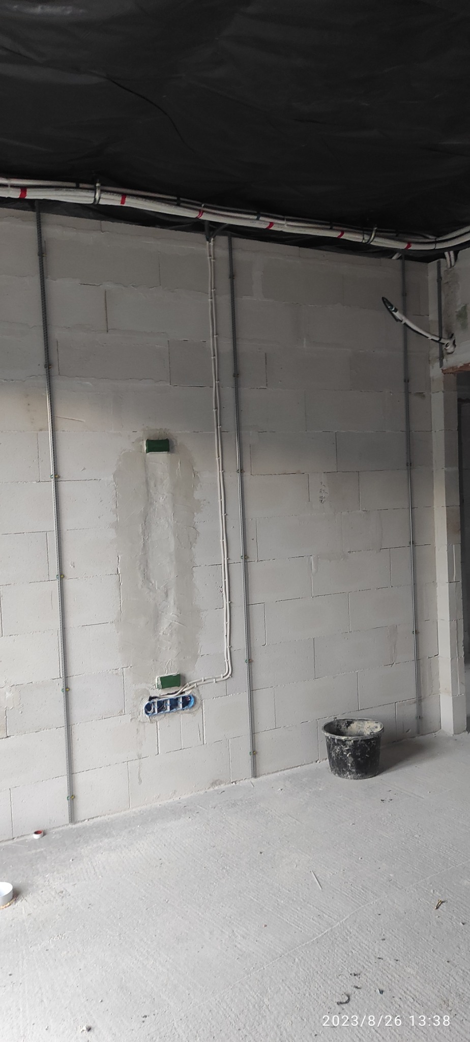 Wewnętrzna instalacja elektryczna w trakcie montażu, widoczne kable w peszlach przymocowane do ściany z betonu komórkowego. Puszkę elektryczne częściowo zamurowane.