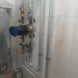 Nowa instalacja hydrauliczna z pompą obiegową LFP, rurami stalowymi i zaworami, zamontowana na ścianie z białych płytek w pomieszczeniu w trakcie prac wykończeniowych.