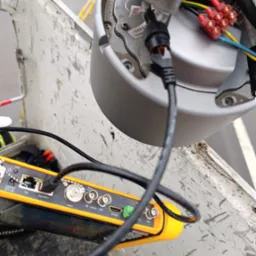 Podłączenie kamery monitoringu za pomocą testera okablowania. Widoczne złącza, kable i kostka elektryczna. Urządzenie w koszu podnośnika.