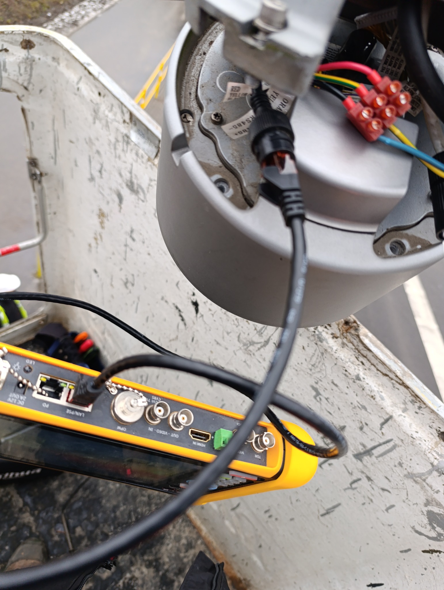 Podłączenie kamery monitoringu za pomocą testera okablowania. Widoczne złącza, kable i kostka elektryczna. Urządzenie w koszu podnośnika.