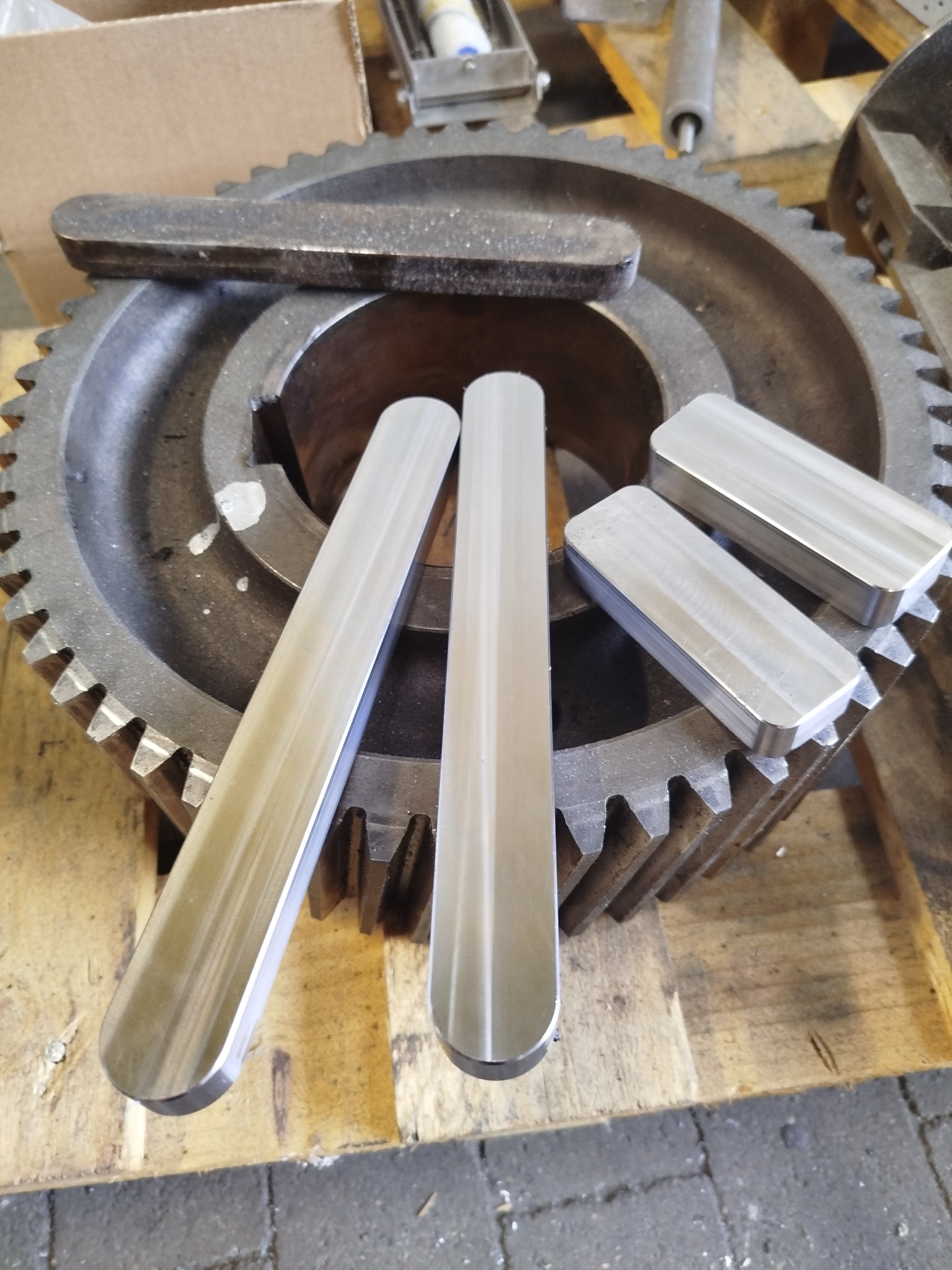 Precyzyjnie obrobione, błyszczące metalowe elementy o gładkiej powierzchni leżą na zębatym kole. Widoczna faktura drewna pod spodem. Detal procesu produkcyjnego.