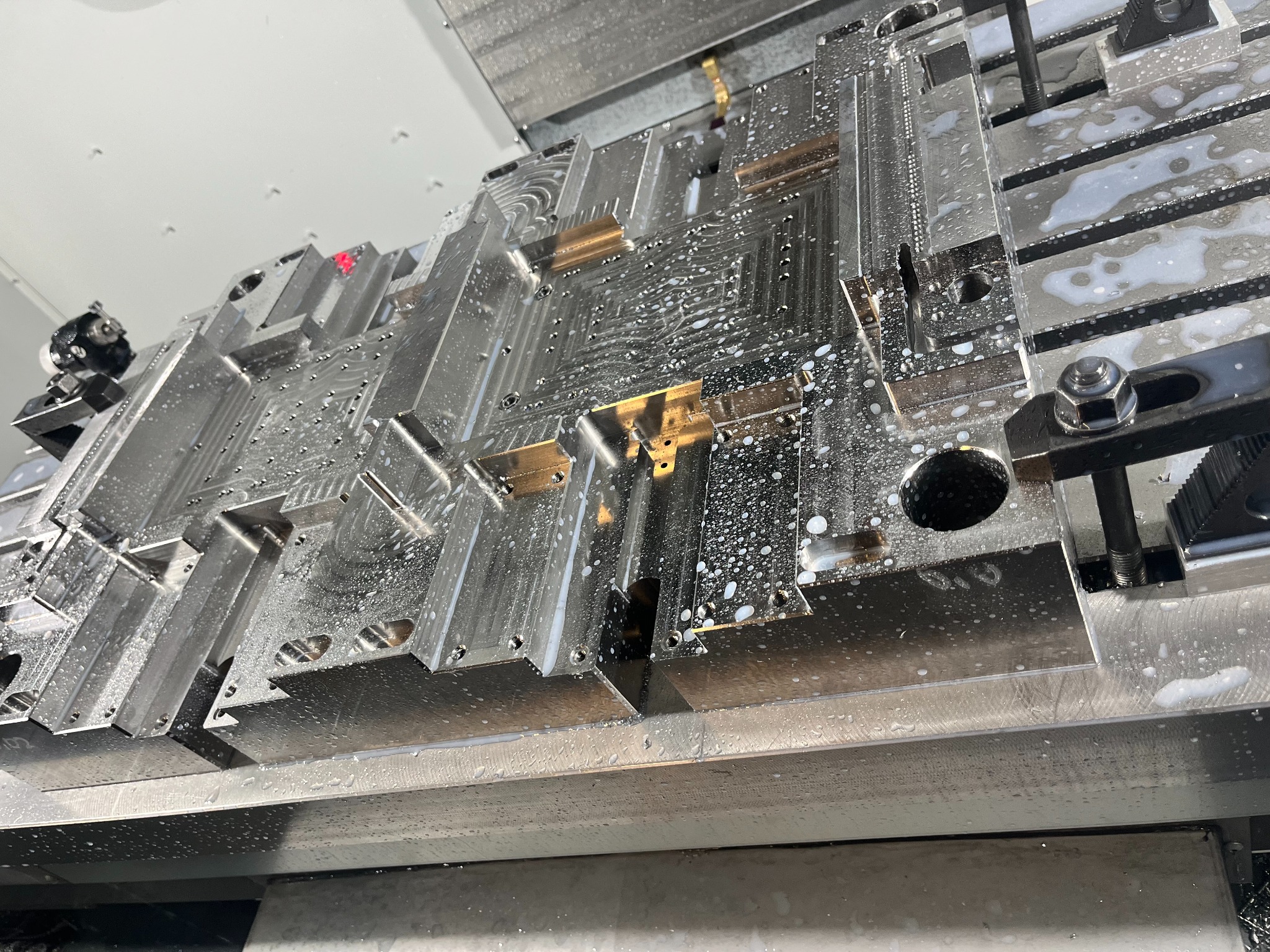 Metalowa forma, prawdopodobnie po obróbce CNC, pokryta chłodziwem, widoczna z bliska pod kątem, detale frezowania.