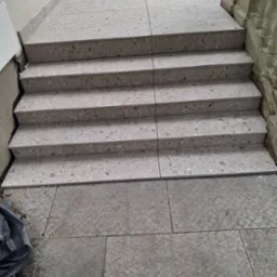 Wykończone schody zewnętrzne z płytek imitujących kamień, prowadzące na taras. Widoczne detale wykończenia i faktura materiału.