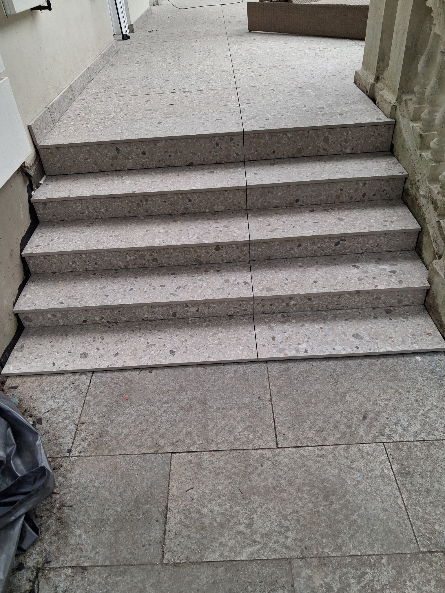 Wykończone schody zewnętrzne z płytek imitujących kamień, prowadzące na taras. Widoczne detale wykończenia i faktura materiału.