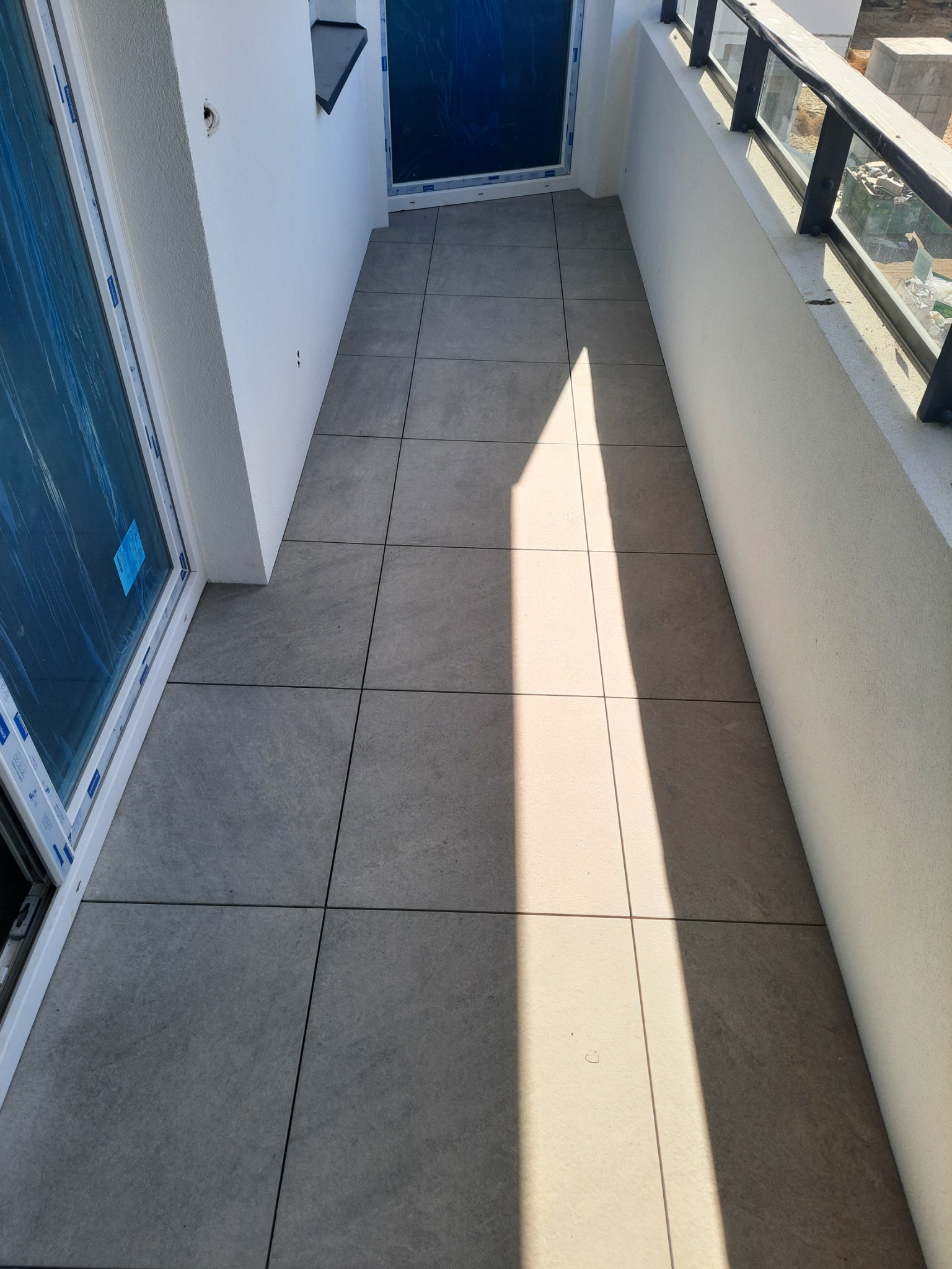 Wykończony balkon z szarymi płytkami podłogowymi, białą balustradą z czarnymi elementami i widokiem na zewnątrz. Nowoczesny design i dbałość o detale.