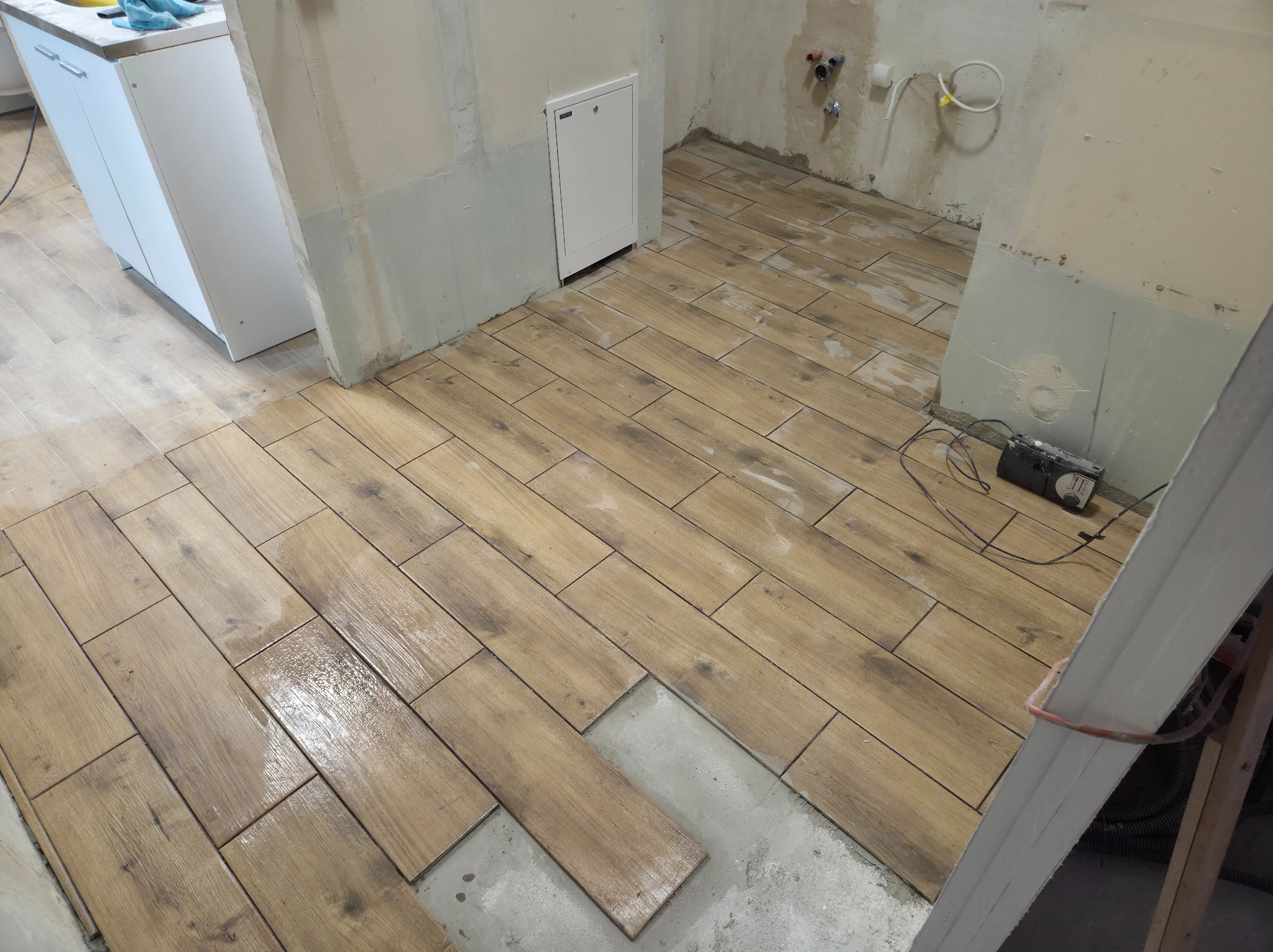 Układanie podłogi z płytek imitujących drewno w trakcie prac. Widoczne narzędzia i fragmenty nieukończonej powierzchni. Płytki ułożone w regularny wzór.