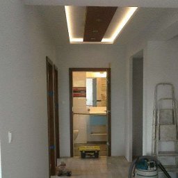 DrigoKomplex B.R.T - Wykończony korytarz z podwieszanym sufitem z oświetleniem LED, widok na łazienkę przez otwarte drzwi, drabina oparta o ścianę.