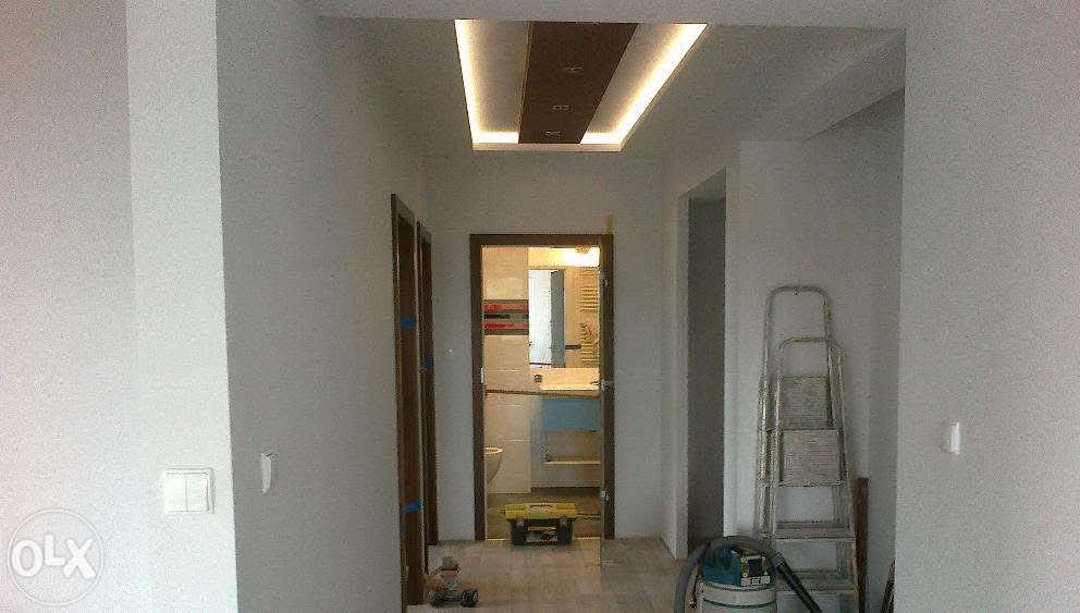 Wykończony korytarz z podwieszanym sufitem z oświetleniem LED, widok na łazienkę przez otwarte drzwi, drabina oparta o ścianę.