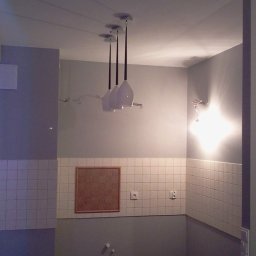 USŁUGI BUDOWLANE DARIUSZ RADOMSKI - Nowoczesna łazienka z białymi płytkami, oświetleniem LED w niszach i wiszącą lampą z trzema kloszami. Minimalistyczny design, szare ściany i akcenty drewniane.