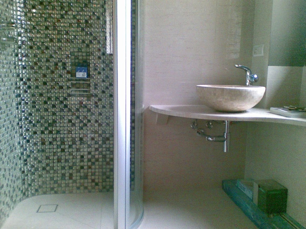 Nowoczesna łazienka z kabiną prysznicową wyłożoną mozaiką i umywalką w kształcie misy na blacie z zaokrąglonym rogiem. Minimalistyczny design, jasne kolory.