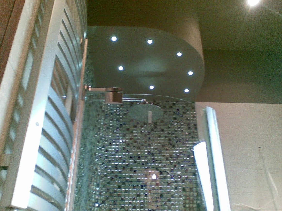 Mozaika w kabinie prysznicowej z deszczownicą, oświetlenie punktowe sufitowe, grzejnik drabinkowy w łazience. Nietypowy kadr z dołu.