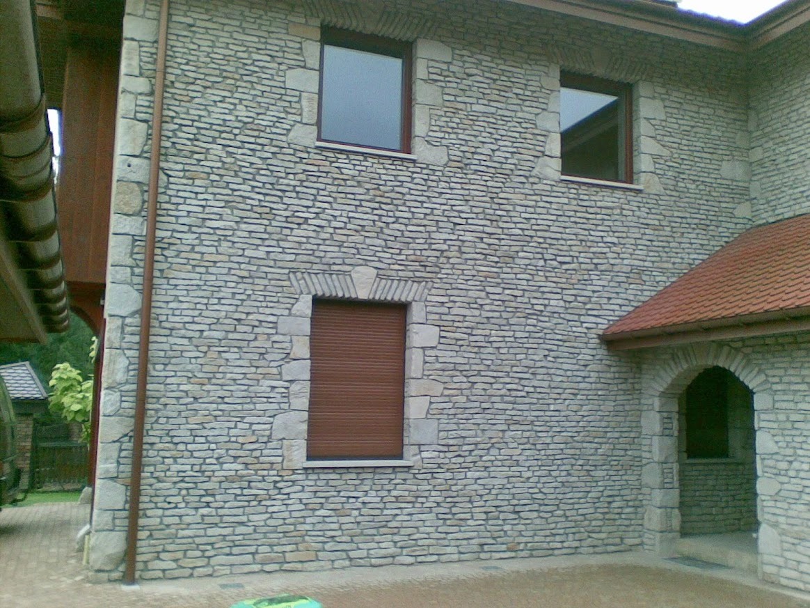 Elewacja budynku wykończona kamieniem naturalnym w odcieniach szarości, z widocznymi oknami i wejściem w kamiennej obudowie. Detal architektoniczny.