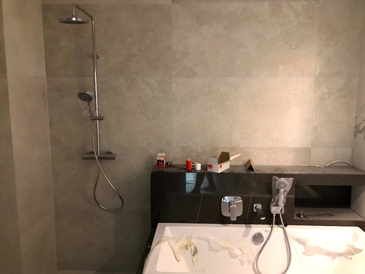 Wykończona łazienka z beżowymi płytkami, chromowaną armaturą i wanną zabezpieczoną folią. Widoczne akcesoria montażowe na blacie.