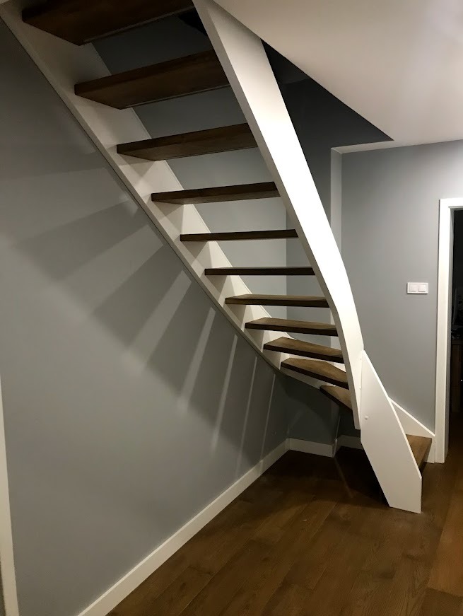 Nowoczesne, drewniane schody wspornikowe z białymi elementami konstrukcyjnymi, zamontowane w szarej klatce schodowej z drewnianą podłogą. Minimalistyczny design.