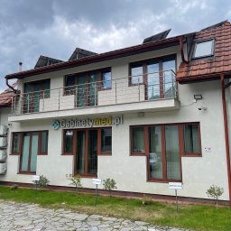 FOOT CARE PIONEERS Olga Legkoszkur - Dwukondygnacyjny budynek kliniki z balkonem i panelami słonecznymi na dachu, widoczny z zewnątrz, z tabliczkami informacyjnymi na trawniku przed budynkiem.