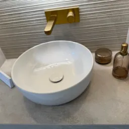 Nowoczesna łazienka: biała umywalka nablatowa, złota armatura i dekoracyjne płytki ścienne z subtelnym wzorem. Minimalistyczny design.