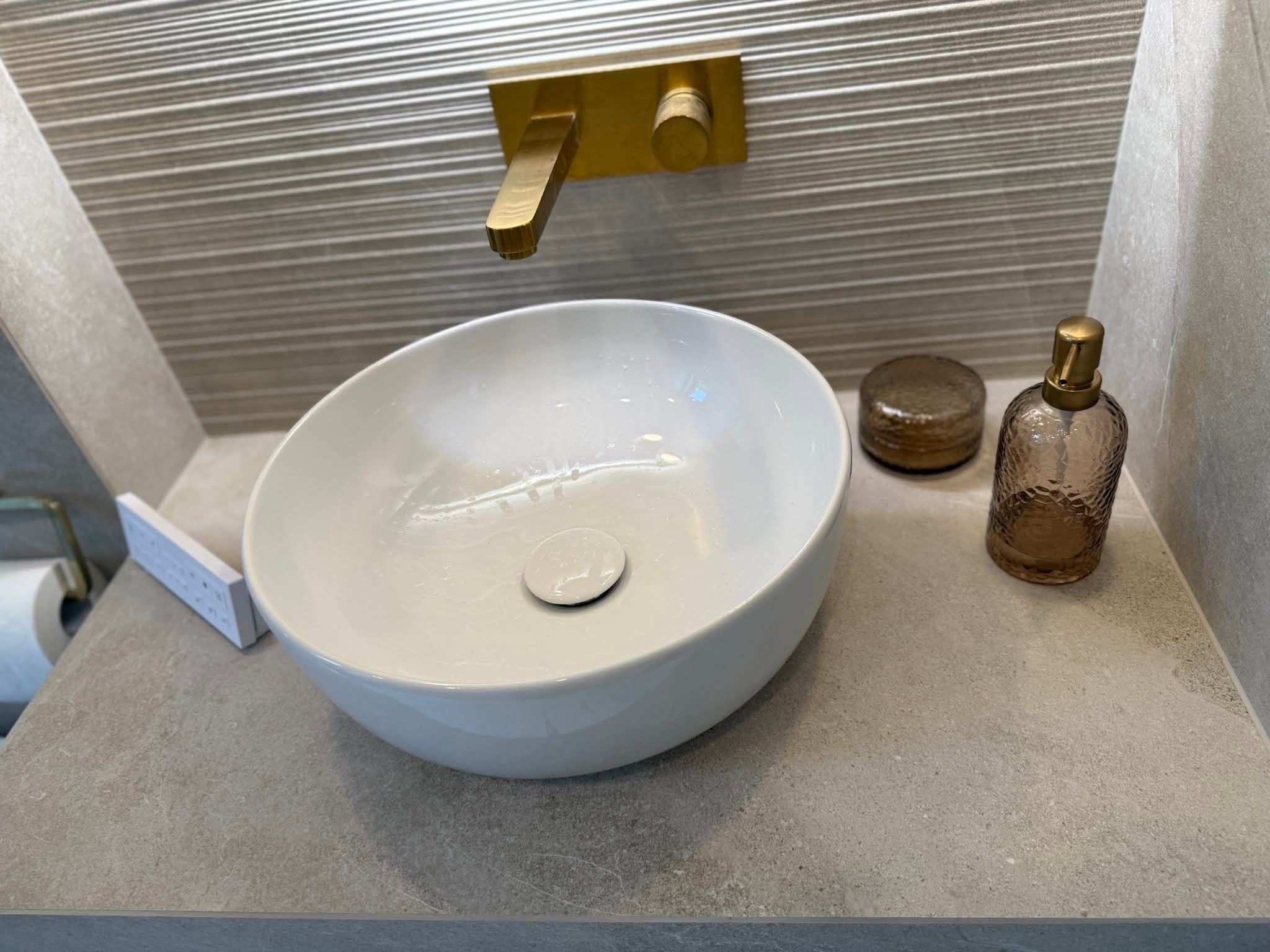 Nowoczesna łazienka: biała umywalka nablatowa, złota armatura i dekoracyjne płytki ścienne z subtelnym wzorem. Minimalistyczny design.