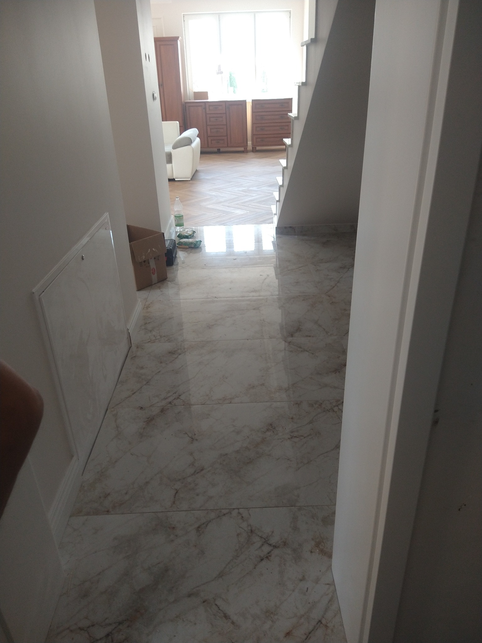 Wykończone marmurowe płytki podłogowe w korytarzu z widokiem na schody i salon. Widoczna skrzynka rewizyjna na ścianie i częściowo widoczne drzwi.