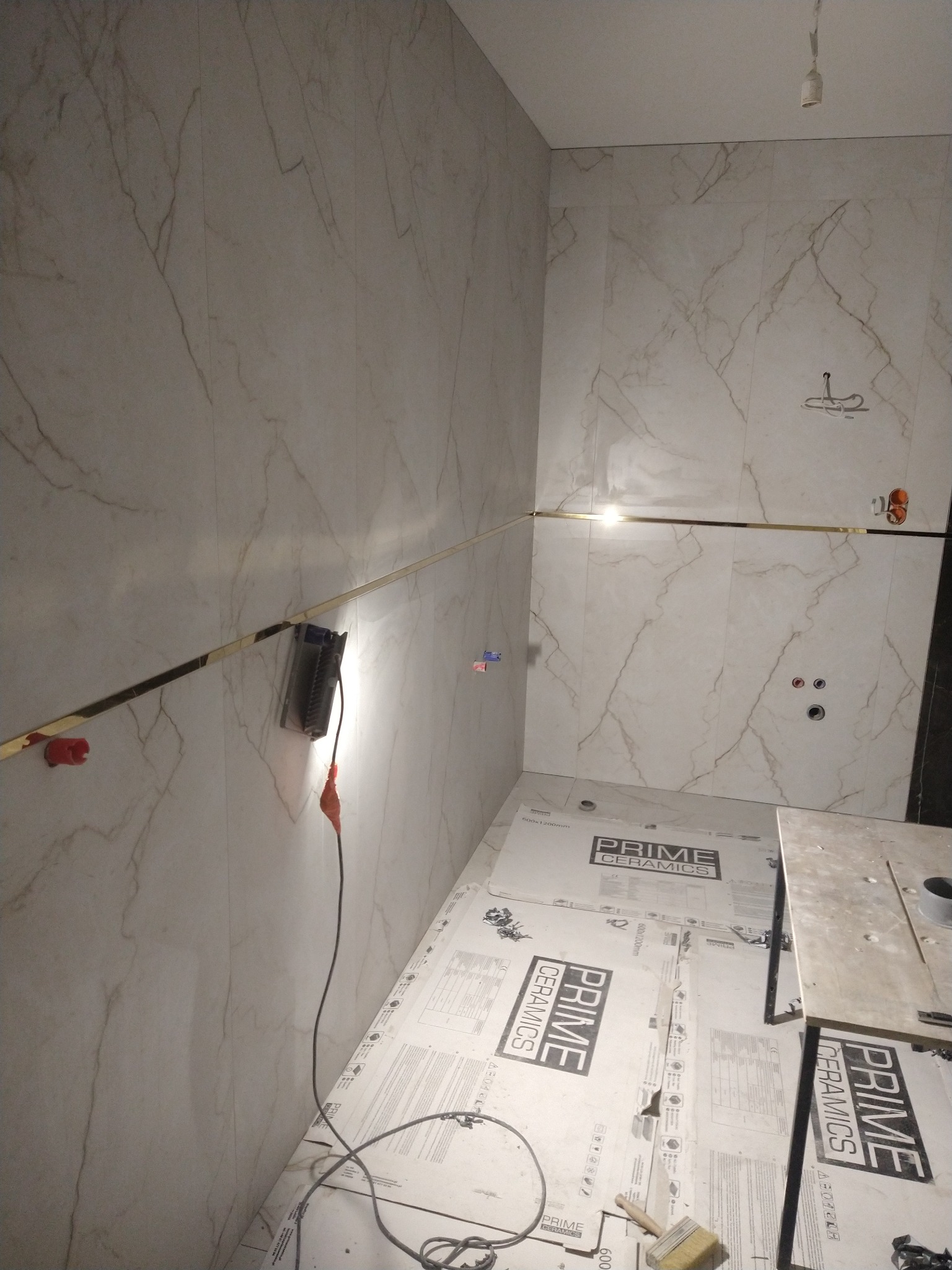 Wnętrze łazienki w trakcie wykańczania: marmurowe płytki na ścianach z listwą dekoracyjną, zabezpieczona podłoga, widoczne narzędzia i akcesoria montażowe.