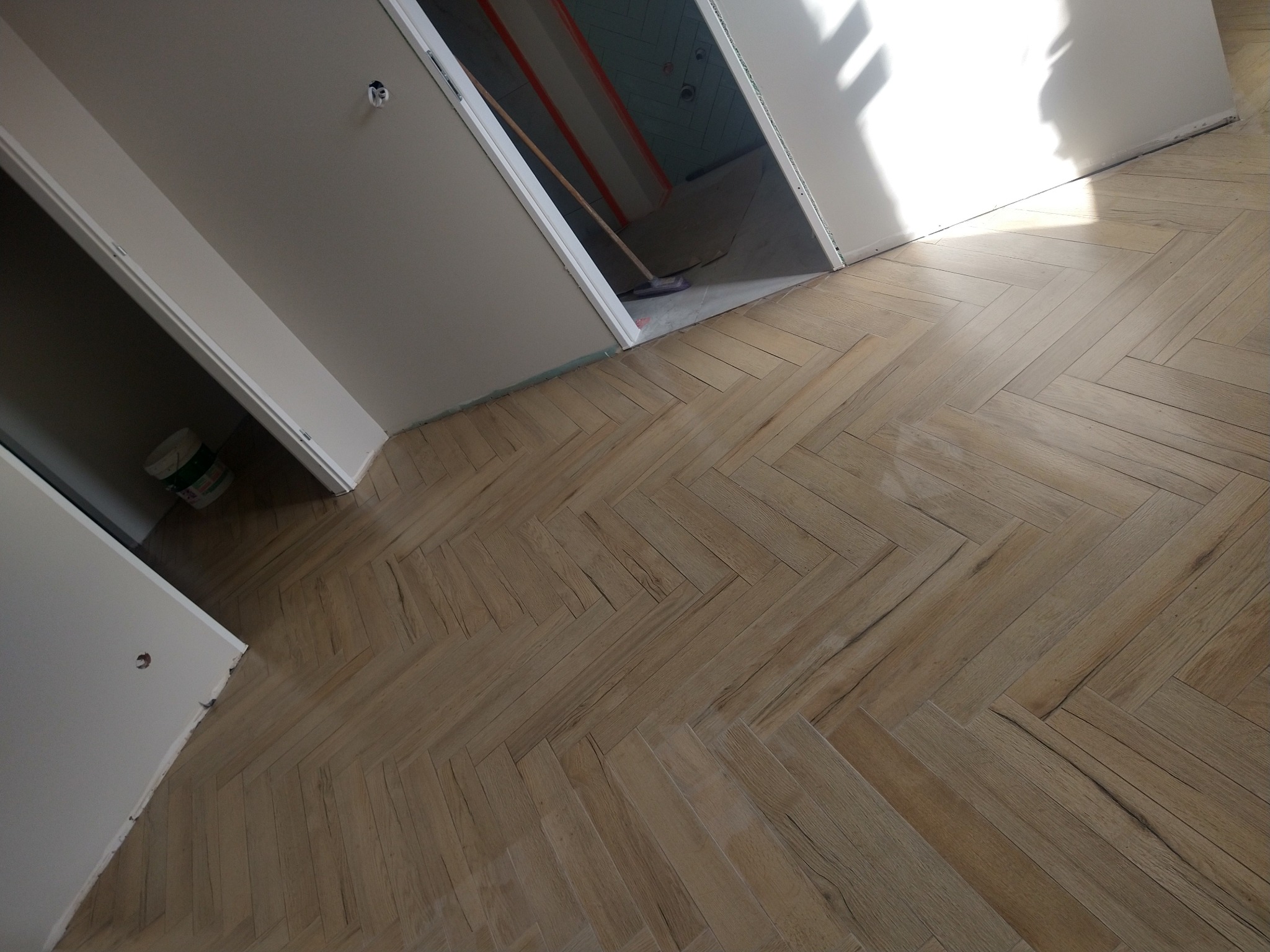 Ukończona podłoga z paneli ułożonych w jodełkę, widoczna z perspektywy pod kątem. W tle fragment pomieszczenia w trakcie prac wykończeniowych.