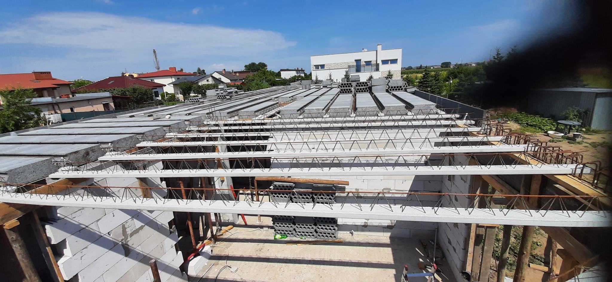 Budowa domu: strop Teriva z pustakami, widok z góry na konstrukcję z betonu i stali, w tle domy jednorodzinne i błękitne niebo.