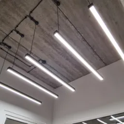 Nowoczesne, podwieszone oświetlenie LED w biurze z surowym, betonowym stropem i widocznymi przewodami. Minimalistyczny design lamp.