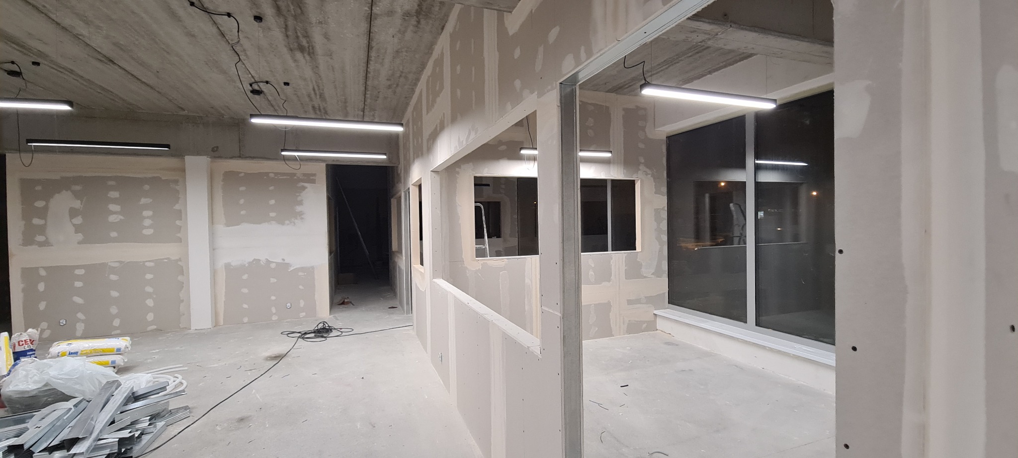 Montaż płyt gipsowo-kartonowych na metalowej konstrukcji w nowo budowanym pomieszczeniu biurowym. Widoczne kable oświetleniowe.