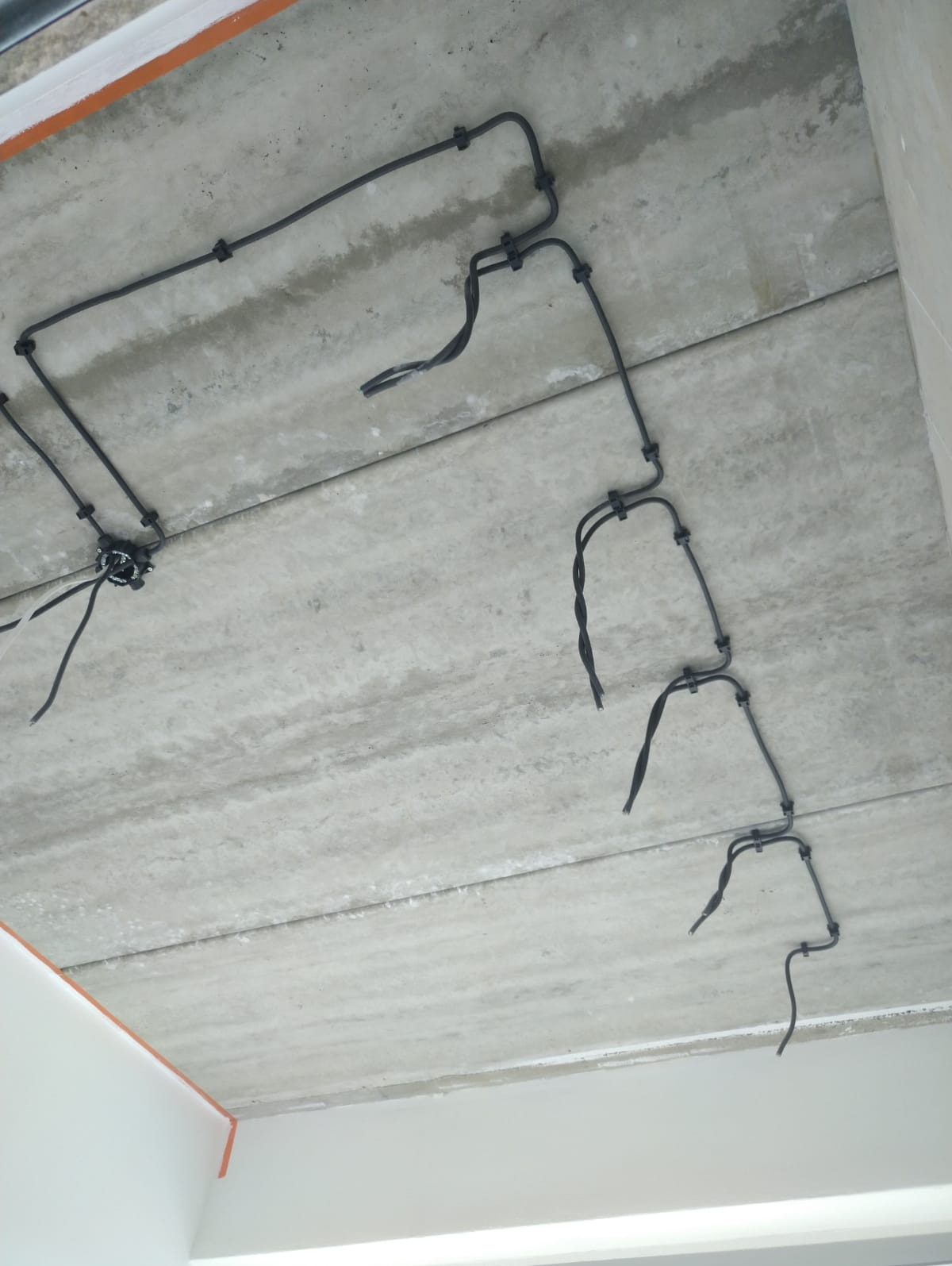 Szara, surowa betonowa płyta stropowa z zamocowanymi przewodami elektrycznymi w peszlach, widoczne złącza. Prace elektryczne w Głogowie.