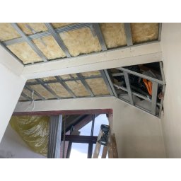 Vadym Davydenko - Montaż metalowej konstrukcji sufitu podwieszanego z izolacją z wełny mineralnej. Widoczna drabina i narzędzia. Prace remontowe w trakcie realizacji.