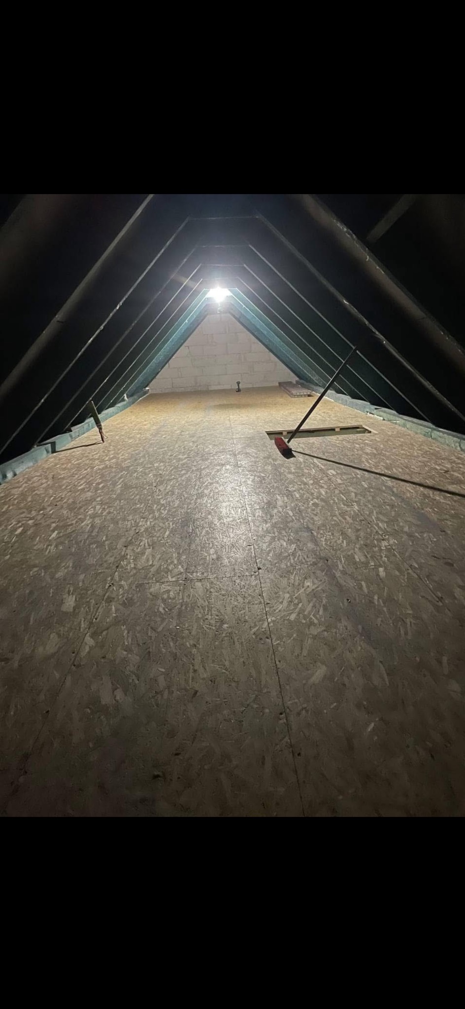 Poddasze z płyt OSB, widoczne krokwie i oświetlenie. Na podłodze leżą narzędzia. Ujęcie z dołu, podkreślające przestrzeń i konstrukcję dachu.