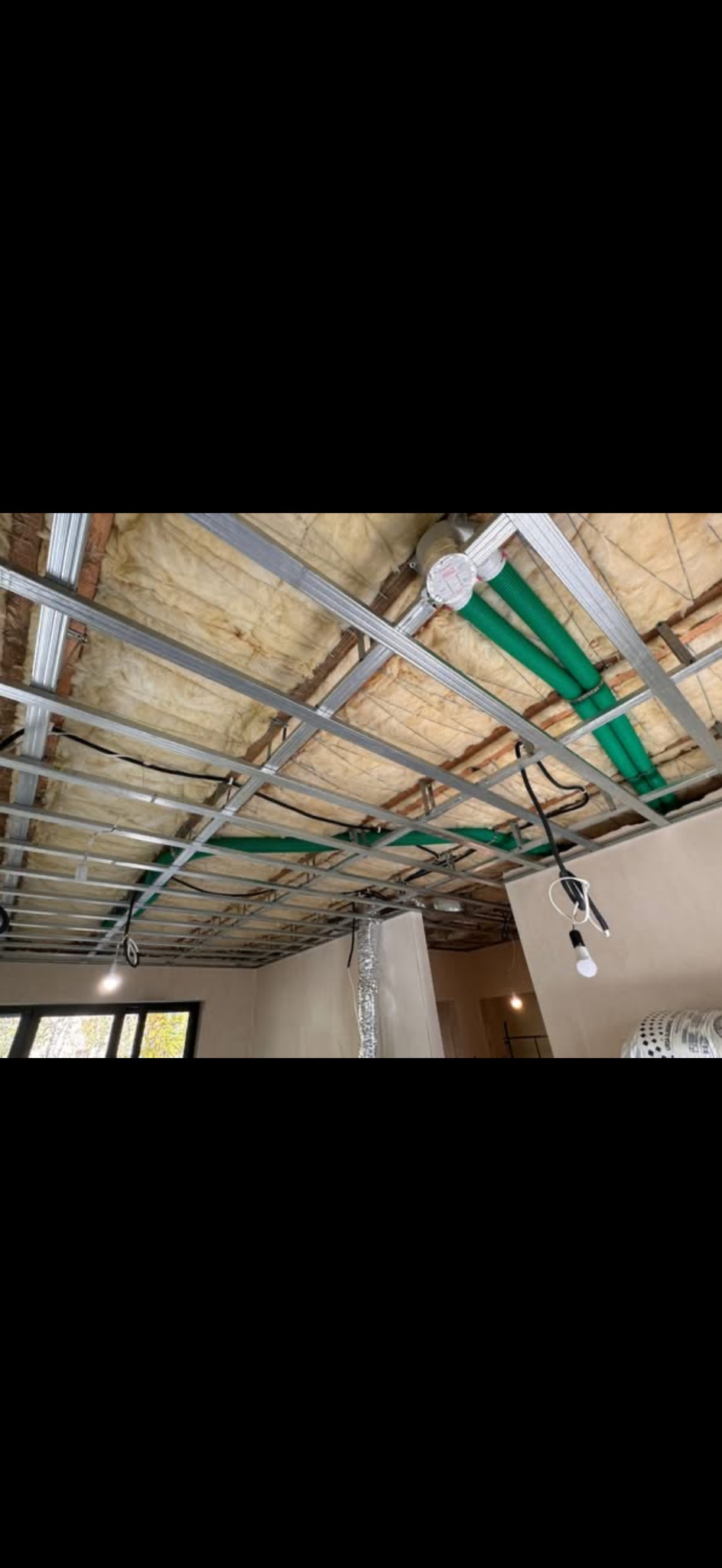 Metalowa konstrukcja sufitu podwieszanego z izolacją i instalacją wentylacyjną w trakcie montażu. Widoczne przewody i oświetlenie tymczasowe.