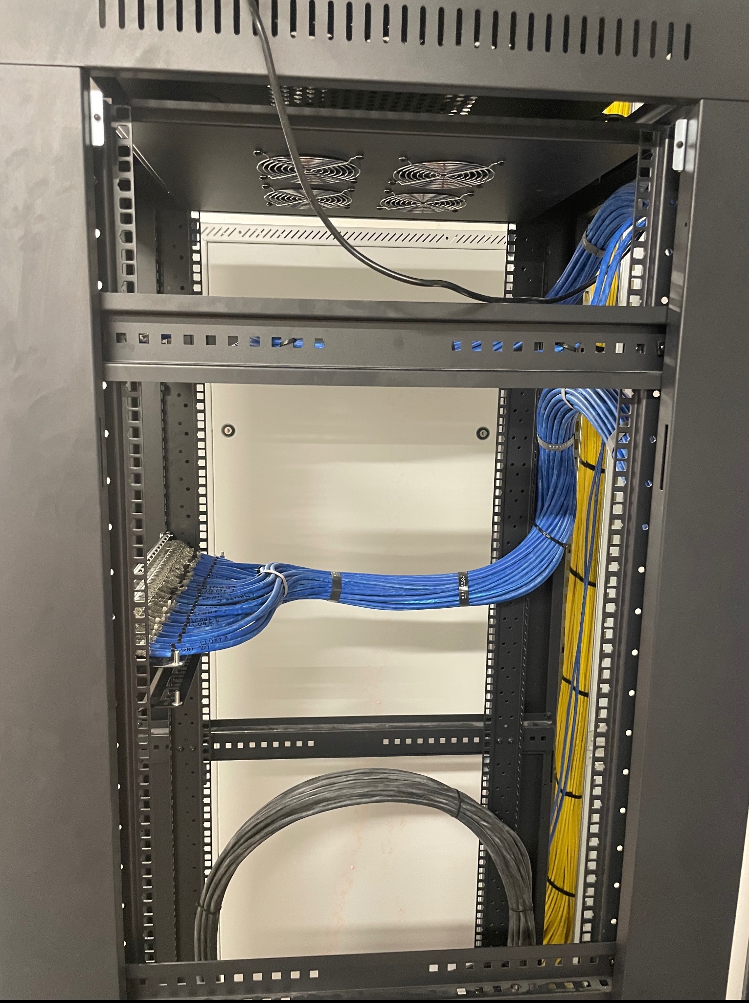 Rzut z góry na szafę rack z uporządkowanymi kablami: niebieskie kable patchcord, żółte kable światłowodowe i czarne kable zasilające. Widoczne wentylatory chłodzące.