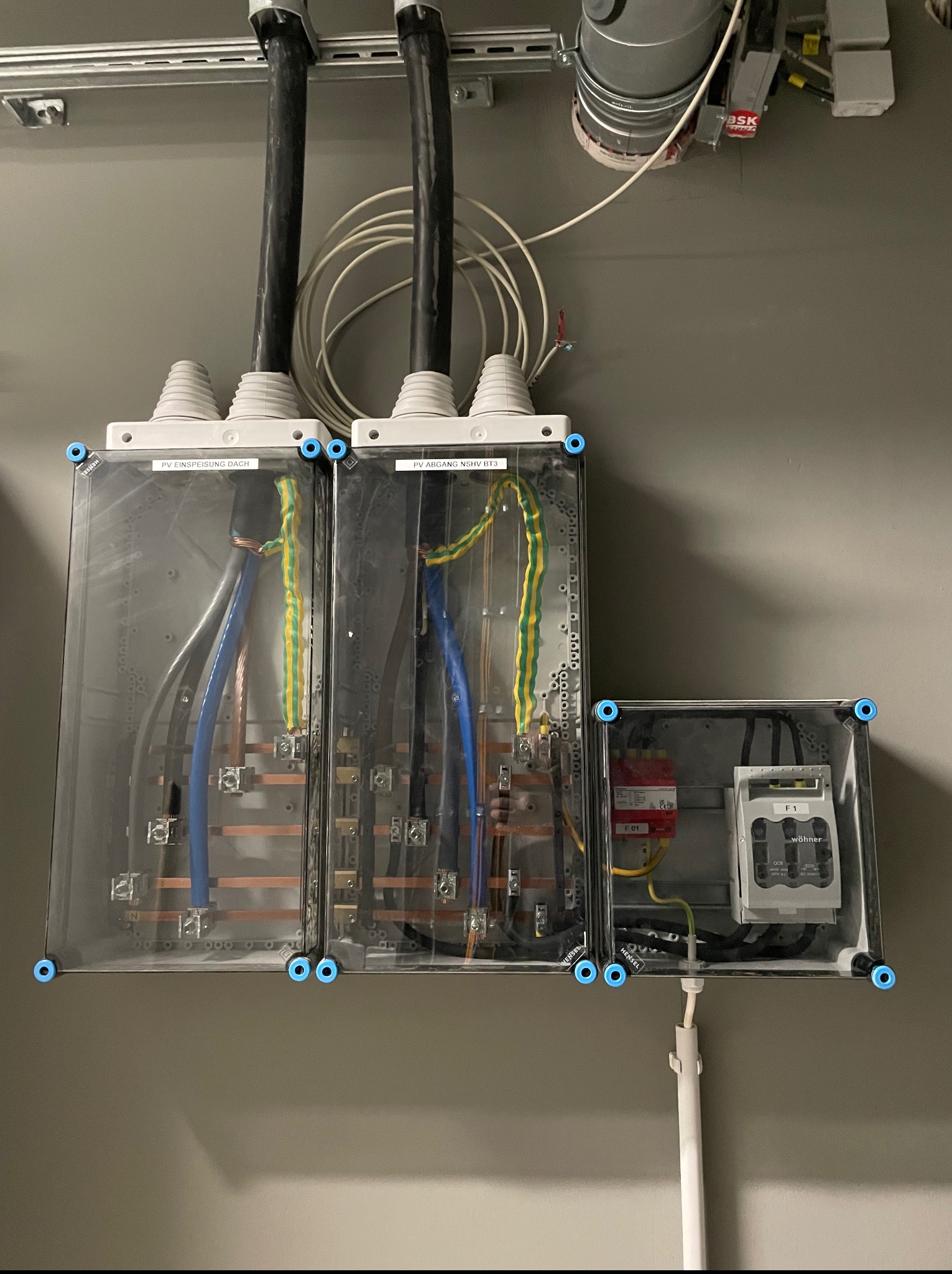 Rozdzielnica elektryczna w obudowie z widocznymi przewodami, bezpiecznikami i oznaczeniami. Instalacja połączona z systemem fotowoltaicznym na dachu budynku.