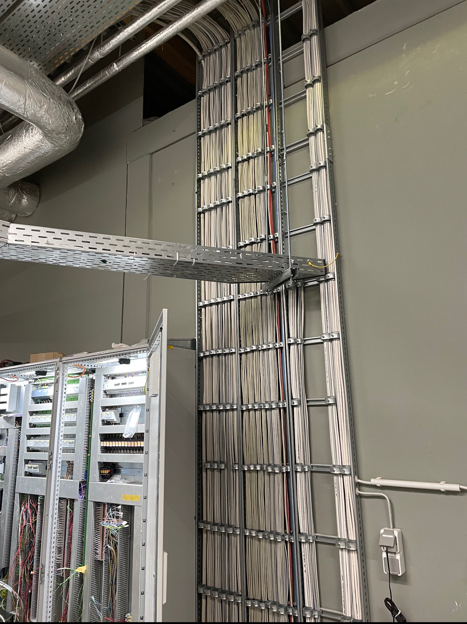 Uporządkowane kable w korytkach i szafa sterownicza z widocznymi przewodami, instalacja elektryczna w szarej tonacji, widok z dołu.