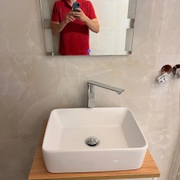 InnerLine Oleh Khomyn - Nowoczesna łazienka z białą, prostokątną umywalką nablatową i chromowaną baterią. W lustrze odbija się mężczyzna robiący zdjęcie telefonem. Widoczne gniazdka elektryczne.