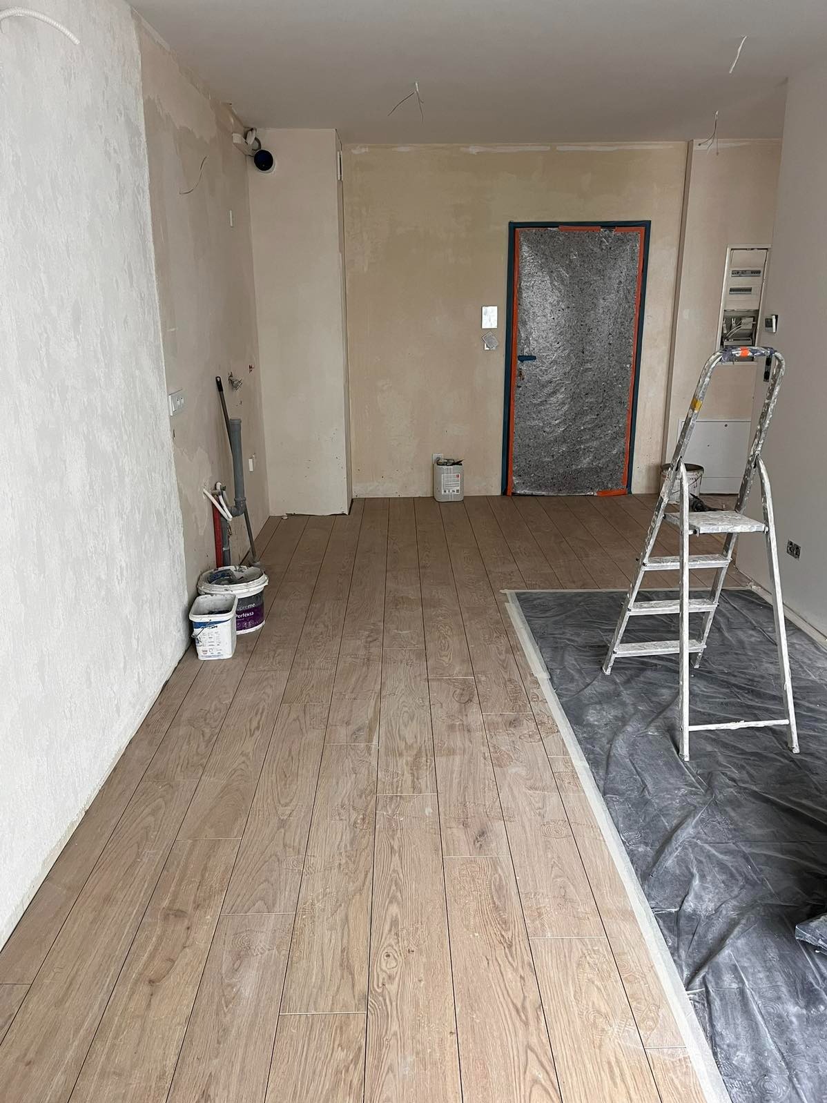 Ukończona podłoga z paneli drewnopodobnych w trakcie prac wykończeniowych, z zabezpieczoną folią częścią podłogi i drabiną w pomieszczeniu.